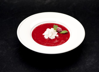 Cold soup with strawberries and raspberry or smoothie in a bowl on a black background