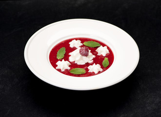 Cold soup with strawberries and raspberry or smoothie in a bowl on a black background