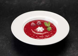 Cold soup with strawberries and raspberry or smoothie in a bowl on a black background
