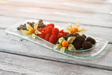 Blackberry and raspberry on plate. Plate with berry dessert. Dessert with flower decoration. Enjoy the summer.