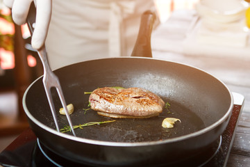 Meat and herb on pan. Hand with meat fork. Add some garlic and herbs. Preparation of duck steak.
