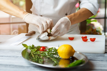 Hands put herbs into fish. Raw fish on cooking board. Chef stuffs dorado fish. Preparation of seafood dish.