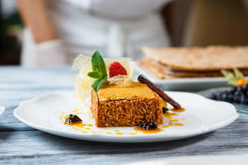 Plate with piece of cake. Cinammon stick on fresh cake. Honey cake on restaurant table. Pastry made of natural ingredients.