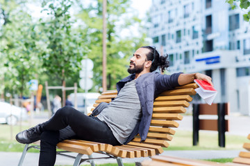 man with notebook and bag on city street bench