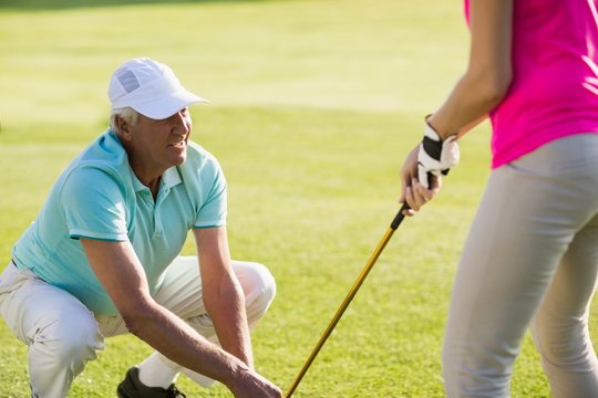 Mature golfer man crouching while teaching woman