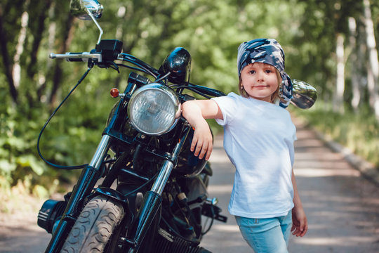 Little girl in a white T-shirt and bandana standing near  motorcycle