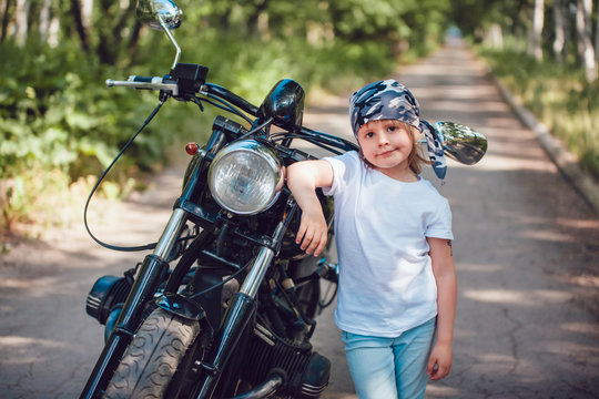 Little girl in a white T-shirt and bandana standing near  motorcycle