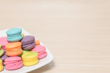 Stack of colorful macaroons cookies in dish on wood background w