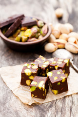 Fototapeta premium Dark chocolate cubes with pistachios on wooden background