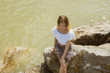 young slender girl is resting on the sea sitting on the rocks
