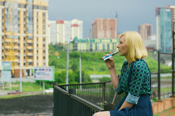 beautiful young girl sitting against a background of cityscape elektronuuyu smokes a cigarette