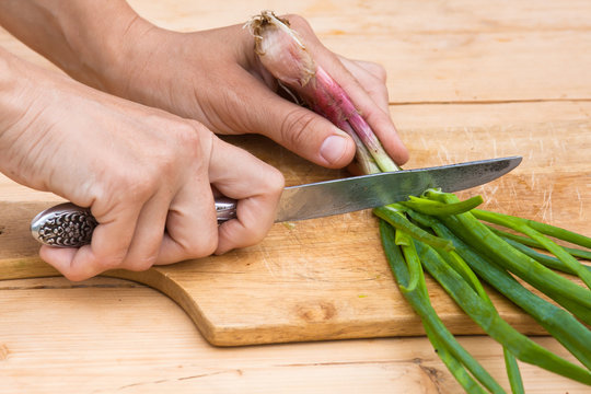 hands chopping green onion on the wooden cutting board