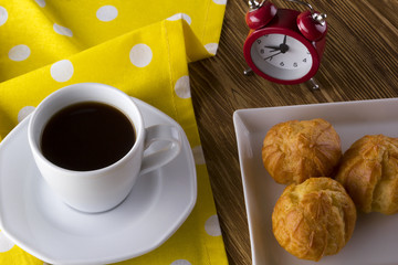 Eclair, coffee cup and alarm clock