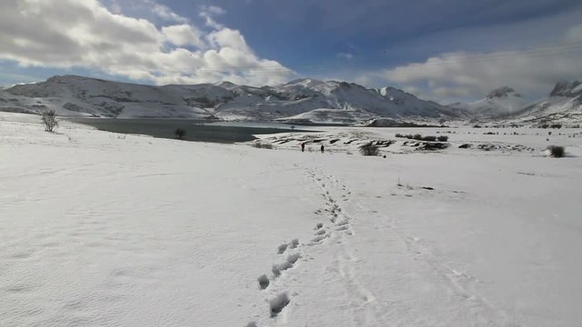 Dos personas en Paisaje Nevado con Lago y huellas en primer plano