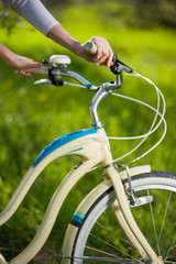 Fototapeta na wymiar Close-up hands of a young woman holding handbrake on vintage bicycle on the blurred background of fresh greenery