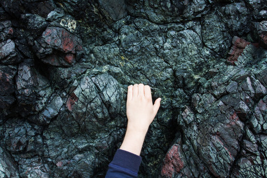 A pair of hands clinging by the fingertips to the side of a harsh, granite rock face.