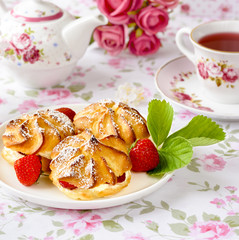 Cream puffs cakes or profiterole filled with whipped cream and served with strawberries on the table