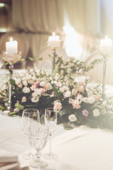 Wedding table set decoratet in banquet restoraunt. Floral composition beige, pink roses flowers, high candle coasters, glass goblets for wine. Atmosphere luxury. Text, free copy space.