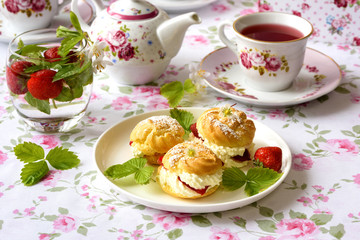 Cream puffs cakes or profiterole filled with whipped cream and served with strawberries on the table