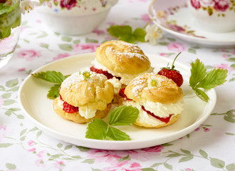 Cream puffs cakes or profiterole filled with whipped cream and served with strawberries on the table