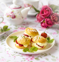 Cream puffs cakes or profiterole filled with whipped cream and served with strawberries on the table