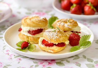 Cream puffs cakes or profiterole filled with whipped cream and served with strawberries on the table