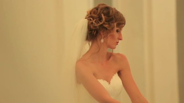 Beautiful sensual blonde bride posing indoors with soft yellow light. Sensual moves of young woman in white gown