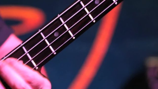 Mano izquierda en el mastil de una guitarra bajo electrico presionando las cuerdas para conseguir notas y acordes
