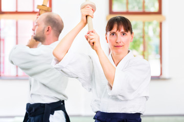 Mann und Frau kämpfen bei Aikido Training in Kampfsportschule mit Holzschwertern