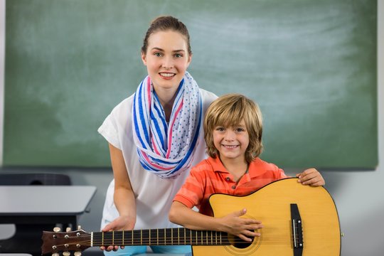 Portrait of young teacher assisting boy to play guitar