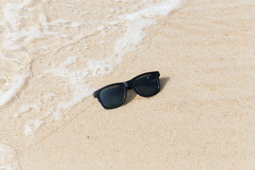Fototapeta na wymiar Black sunglasses on beach in water