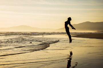 Girl jumping at sunset on a clear sand beach silhouette
