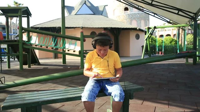 Young boy with  earphone using digital tablet at the playground