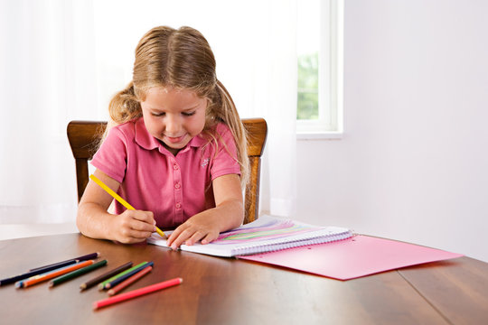 Education: Cute Girl Drawing Rainbow At Table With Colored Penci