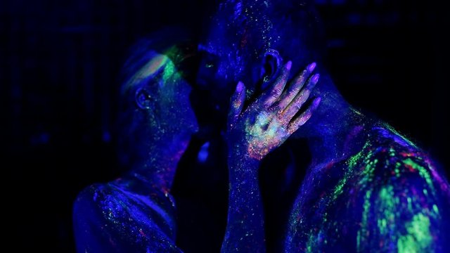 Woman's hand erotically slips on the man's chest under ultraviolet light.