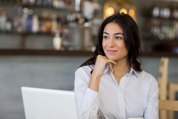 Fototapeta premium Thoughtful businesswoman sitting on table with laptop