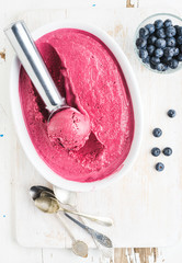 Homemade bluberry ice cream and scooper in mold served with fresh berries, silver spoons on white rusric wooden background