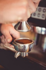 Hands holding tamper with coffee powder