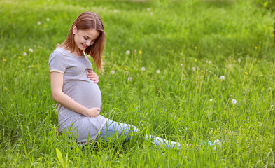 Fototapeta premium Beautiful pregnant woman sitting on grass
