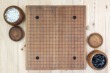 Handicap four stones on go game board with two bowl for black and white over wooden table Top view