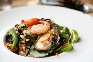 spaghetti with prawns and seafood on white plate, black spaghetti with seafood on table in restaurant, spicy spaghetti in food festival, italian food by spaghetti seafood, international food.