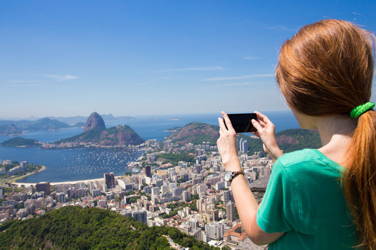 girl tourist takes a picture of Rio landscape with smartphone