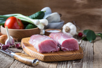 Raw pork tenderloin and vegetables on rustic wooden table