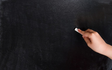 Naklejka premium Child hand writing with chalk on empty chalkboard
