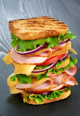 Big sandwich with ham and vegetables on dark wood background