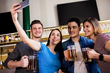Young friends taking selfie while holding beer mug 