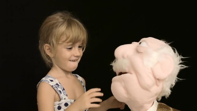 A lovely little girl hugs and kisses a puppet shaped as an old man.