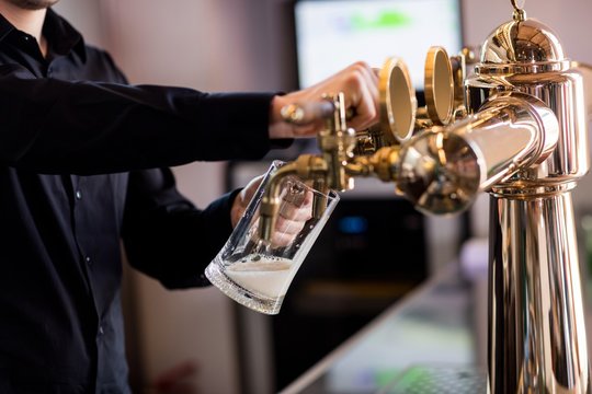 Bartender pouring beer from faucet in pint glass