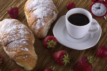 Alarm clock and breakfast with strawberries, coffee , croissant.
