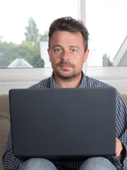 Man on laptop on sofa at home working